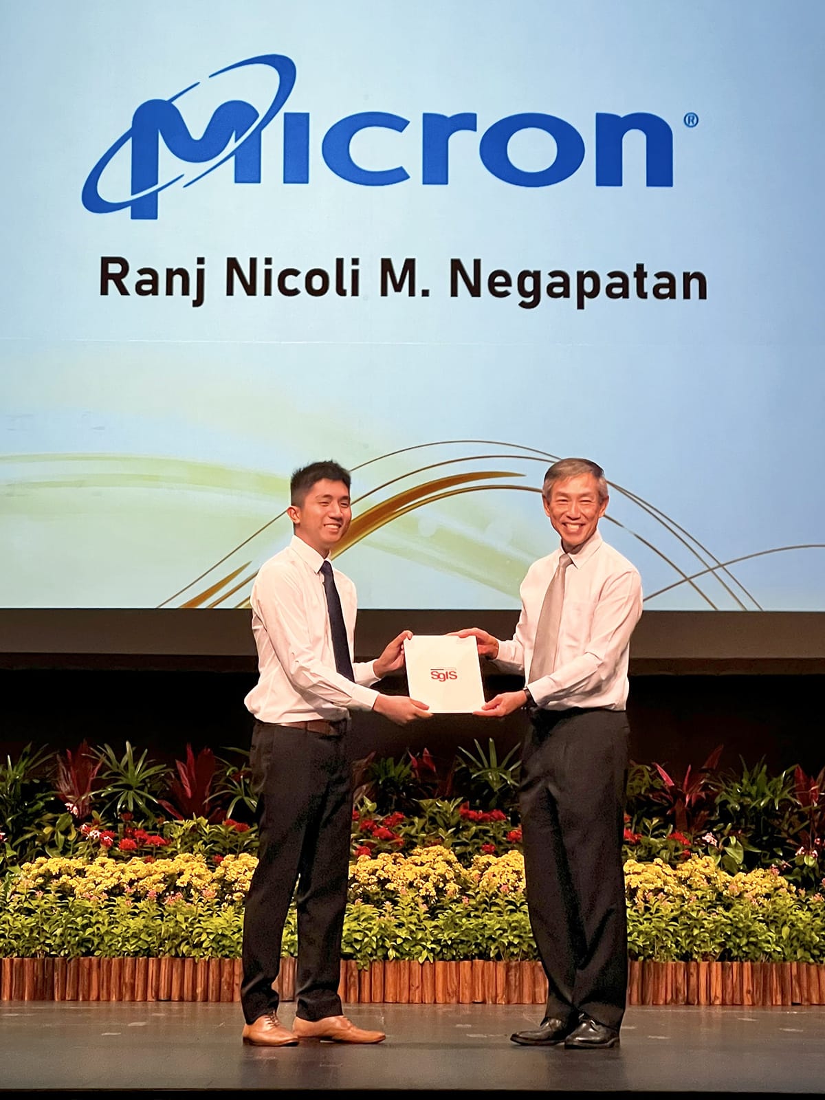 Ranj Nicoli M. Negapatan receives a certificate on stage from an older man, in front of a Micron logo screen with flowers below.